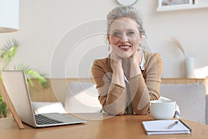 Middle aged woman sitting at a table with a laptop and looking at the camera smiling