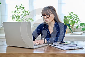 Middle aged woman sitting at workplace in home office, holding pet parrot on shoulder
