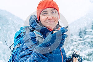 Middle-aged woman smiling, looking at camera drinking a hot drink from thermos flask dressed warm down jacket while she trekking