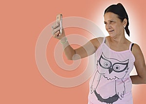 A middle-aged woman smiling and taking a selfie using her android phone