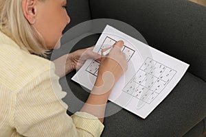 Middle aged woman solving sudoku puzzle on sofa at home