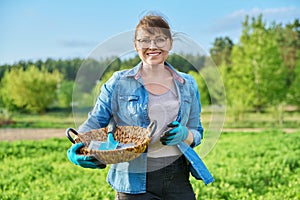 Middle-aged woman in spring garden, in gloves with shovel and seeds in packs