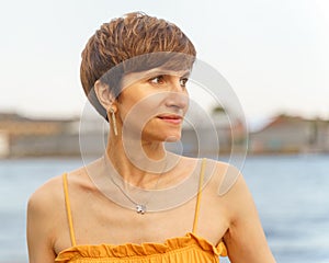 Middle-aged woman standing by river in city embankment, enjoing summer