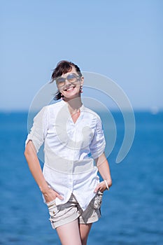 Middle aged woman stands with hands in pockets against sea