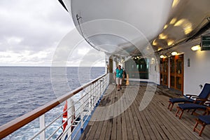 Middle aged woman strolling along teak lined Promenade Deck of modern cruise ship on a grey stormy day