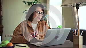 Middle aged woman talk about project strategy on laptop video call in living room. Motivated senior