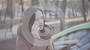 A middle-aged woman talking on the phone near the car