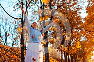 Middle-aged woman throwing leaves in autumn forest. Senior woman having fun outdoors