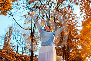 Middle-aged woman throwing leaves in autumn forest. Senior woman having fun outdoors