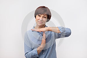 Middle aged woman tired and bored, making a timeout gesture, needs to stop because of work stress, time concept photo