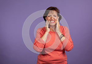 Middle Aged woman with TMJ pain holding her jaw and making a pained expression