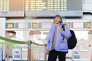 Middle aged woman traveler with backpack at public airport terminal after check in at airline services desks. Active