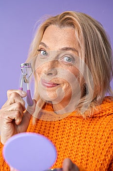 Middle aged woman using eyelash curler while looking at the camera