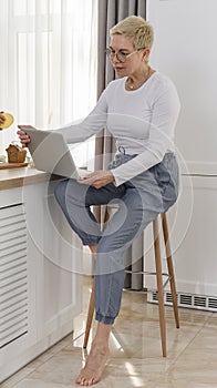 Middle aged woman using laptop at kitchen and looking for recipe online