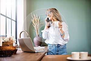 Middle aged woman using laptop and mobile phone while standing in the kitchen
