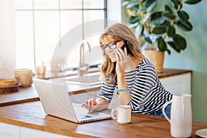 Middle aged woman using laptop and mobile phone while working from home