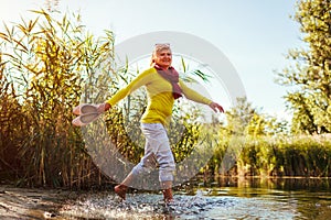 Middle-aged woman walking on river bank on autumn day. Senior lady having fun in the forest enjoying nature