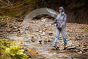 Middle-aged woman walking on river bank on spring day. Senior lady in forest enjoying nature