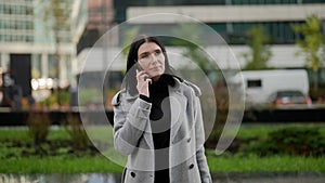 middle aged woman is walking on street and answering on mobile call, portrait of successful lady
