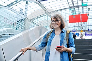 Middle-aged woman walking up stairs, near escalator in modern station buildin