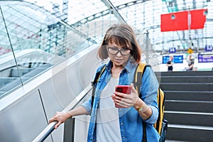 Middle-aged woman walking up stairs, near escalator in modern station buildin