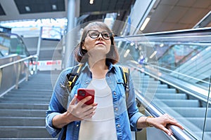 Middle-aged woman walking up stairs, near escalator in modern station buildin