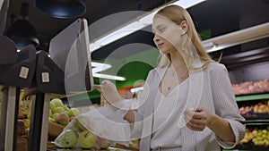 Middle-aged woman weighs a bag of apples in the supermarket.