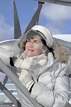 Middle-aged woman in a winter white jacket on the gangplank by a turboprop aircraft