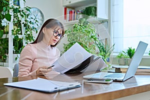 Middle-aged woman working remotely in home office, at workplace with computer