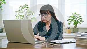 Middle-aged woman working typing on computer laptop in home office