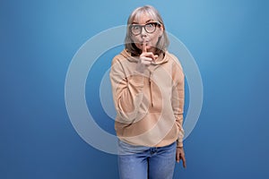 a middle-aged woman in a youth outfit asks to be quieter on a studio background with copy space