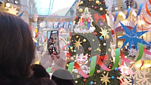 Middle-aged women, Caucasoid, brunette in dark jacket, taking pictures on smartphone in shopping mall christmas