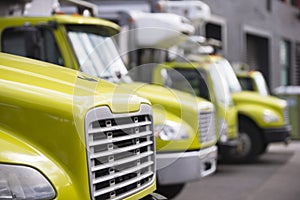 Middle class semi trucks with box trailers for moving and delivery services standing in row in warehouse dock waiting for