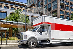 Middle duty rig semi truck with long box trailer with over roof compartment standing on the urban city street with multilevel photo