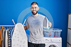 Middle east man with beard holding electric iron smiling and laughing hard out loud because funny crazy joke