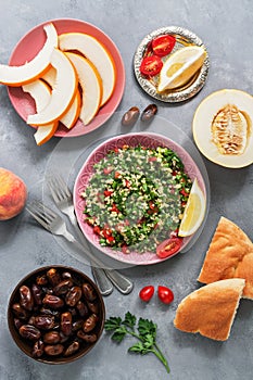 Middle Eastern and Arab food tabbouleh salad, pita, melon, peach and dates on a gray background. Top view, flat lay