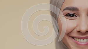 Middle eastern beauty. Half face portrait of young happy muslim lady smiling to camera, beige background, empty space