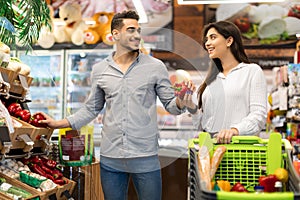 Middle Eastern Couple Choosing Vegetables During Grocery Shopping In Supermarket