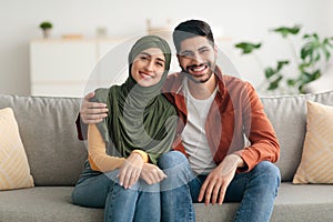 Middle Eastern Couple Hugging Sitting On Sofa Smiling At Home