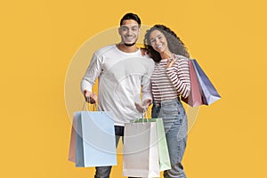 Middle Eastern Couple Posing With Shopping Bags In Hands Over Yellow Background
