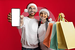 Middle Eastern Couple In Santa Hats Holding Blank Smartphone And Shopping Bags