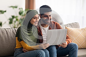 Middle Eastern Couple Using Laptop Sitting In Living Room Indoor