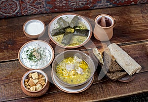 Middle Eastern cuisine dishes in ceramic plates on a wooden table. Chicken soup, dolma with grape leaves, tzatziki, Greek yogurt,