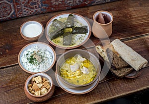 Middle Eastern cuisine dishes in ceramic plates on a wooden table. Chicken soup, dolma with grape leaves, tzatziki, Greek yogurt,