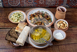 Middle Eastern cuisine dishes in ceramic plates on a wooden table. Soup with mushrooms and herb, pork stew, salad with cabbage and