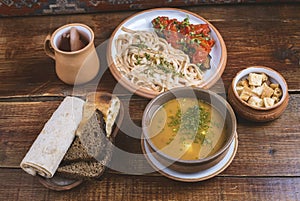 Middle Eastern cuisine dishes in ceramic plates on a wooden table. Vegetable soup with herbs, roasted eggplants and tomatoes with