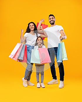 Middle-Eastern Family Holding Shopping Bags Standing On Yellow Studio Background
