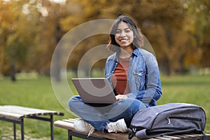 Middle Eastern Female Student With Laptop On Laps Sitting On Bench Outdoors