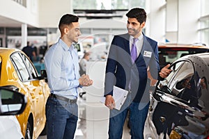 Middle-eastern guy choosing new car, having conversation with sales manager