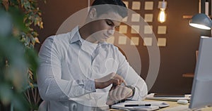 Middle Eastern guy using smart watch touching screen using modern gadget in office in evening